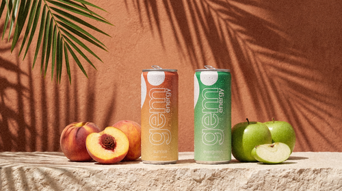 Gem Energy Sunrise and Evergreen cans on a sunlit stone ledge with peaches and green apples