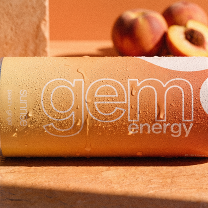 Close-up of a chilled Gem Energy Sunrise can lying on its side next to fresh peaches