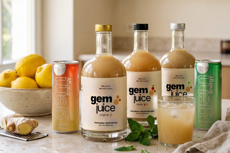 Gem Juice Original, Apple and Mint bottles with Gem Energy Sunrise and Evergreen cans and a glass of ginger drink on a kitchen counter